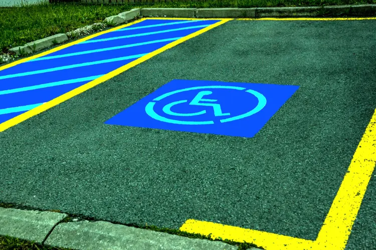 ADA compliant parking space with blue wheelchair symbol and diagonal blue access aisle striping, bordered by yellow curb paint