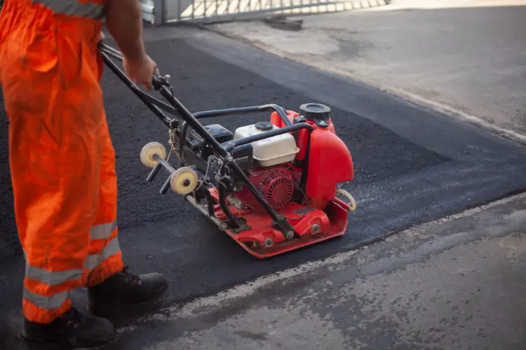 Worker using plate compactor to finish asphalt pothole patc