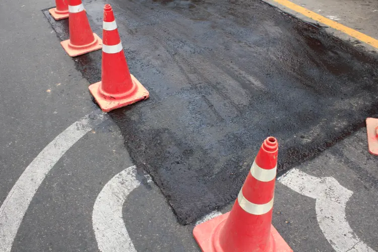 Freshly patched asphalt pothole with safety cones marking the work area