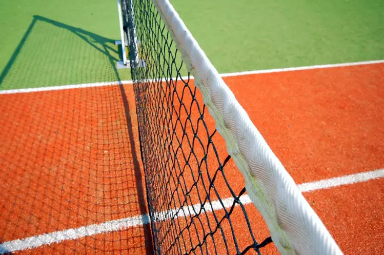 Close-up of tennis net post on a clay court with white boundary lines